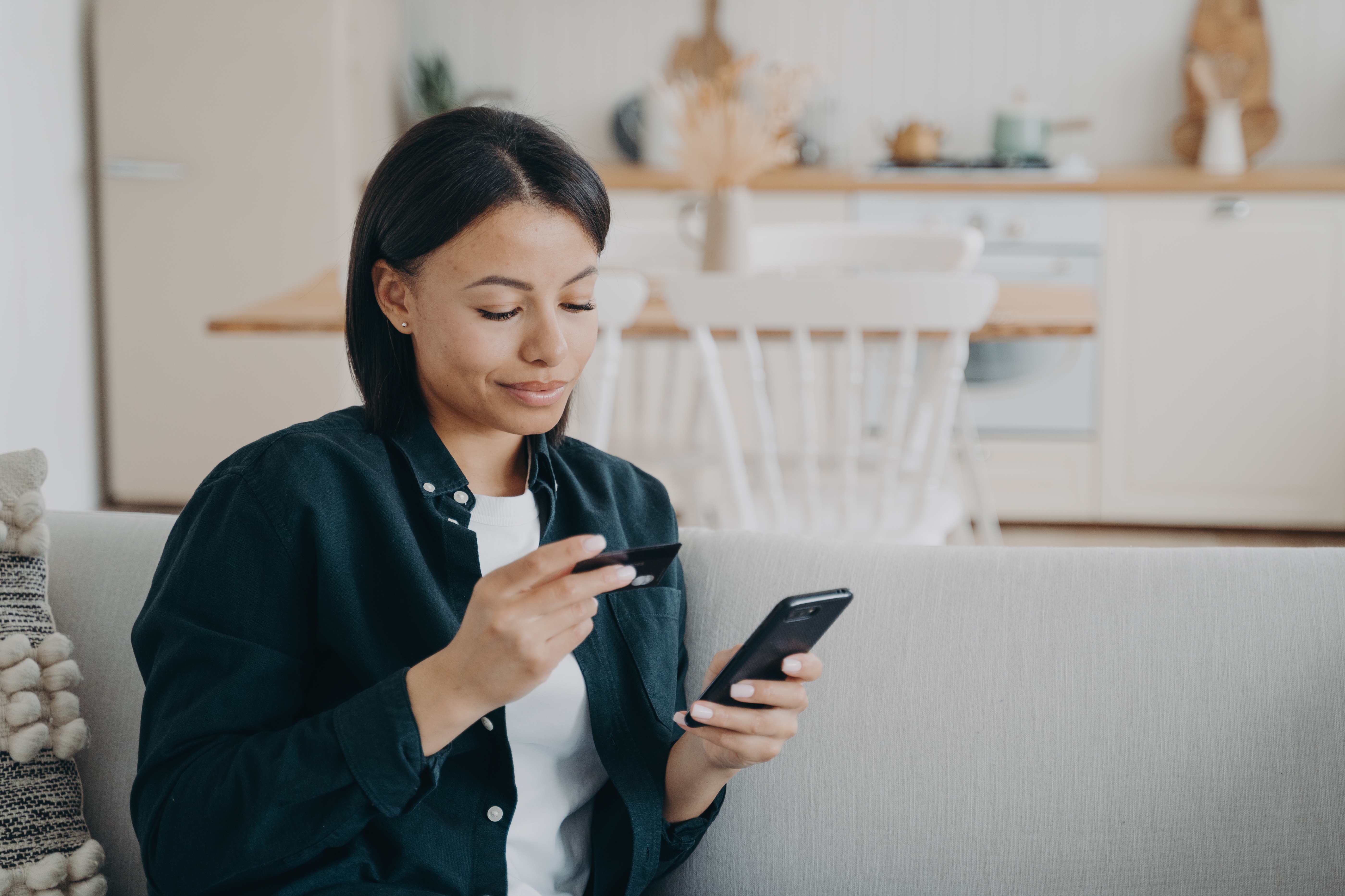 Smiling female holding bank credit card, smartphone, using online banking service at home. E-banking